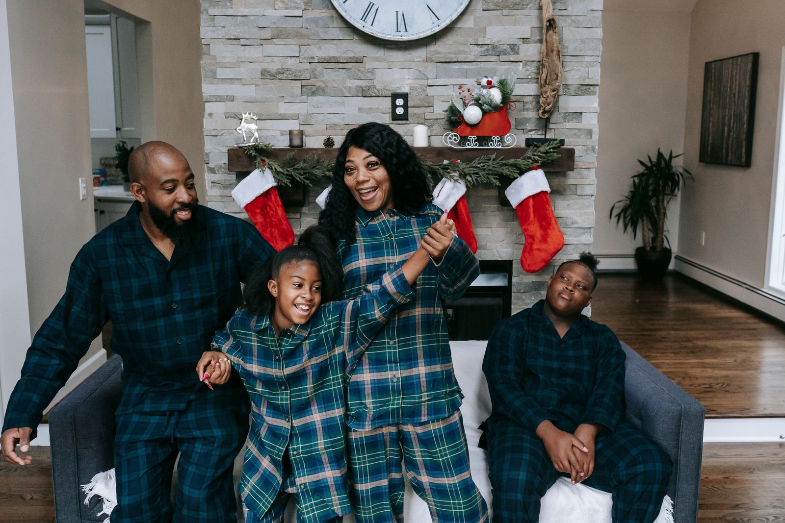 Family in matching green holiday plaid pajamas celebrating in front of their festive fireplace