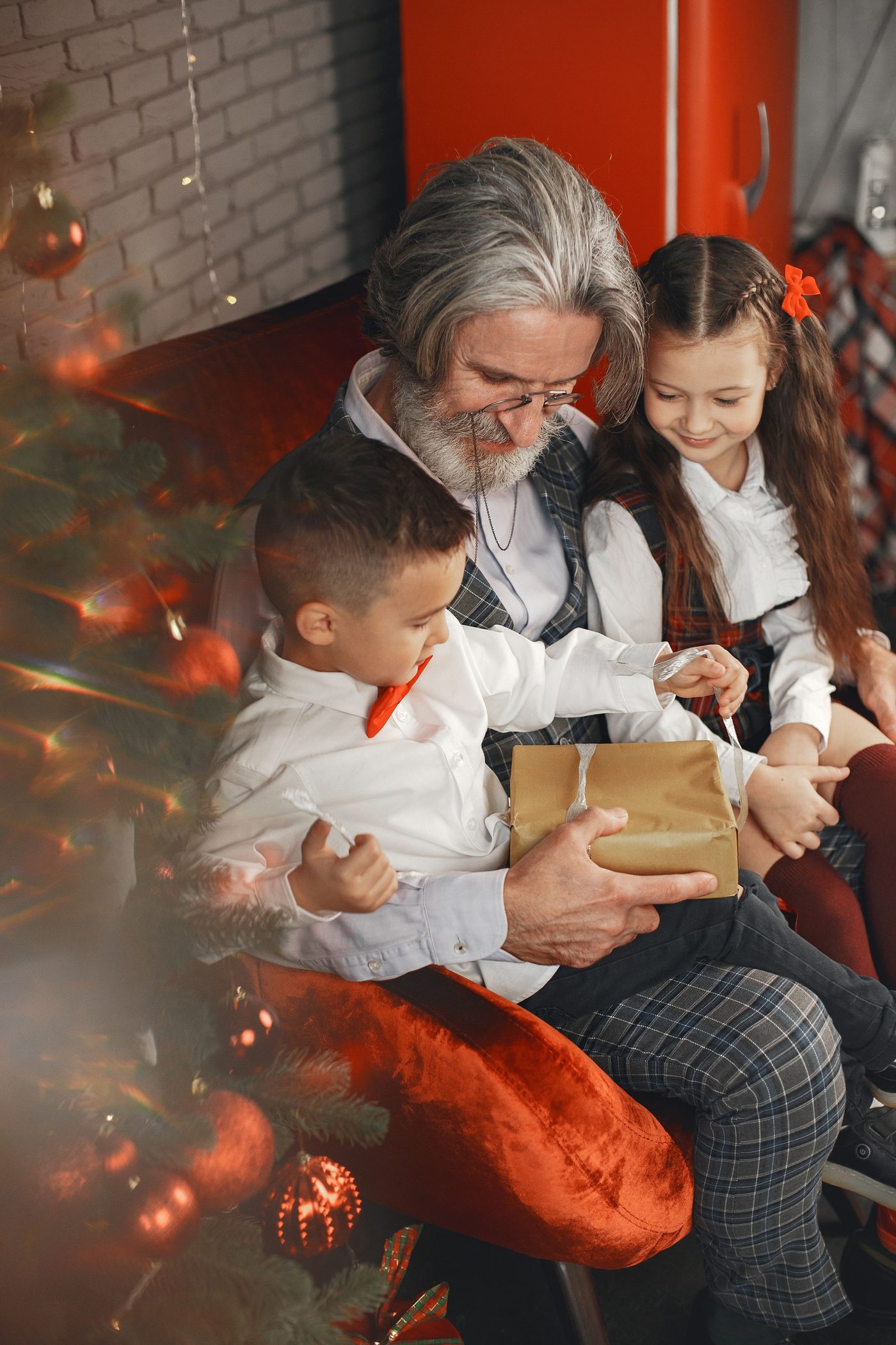 Grandfather and children unwrapping a Christmas gift together beside the holiday tree