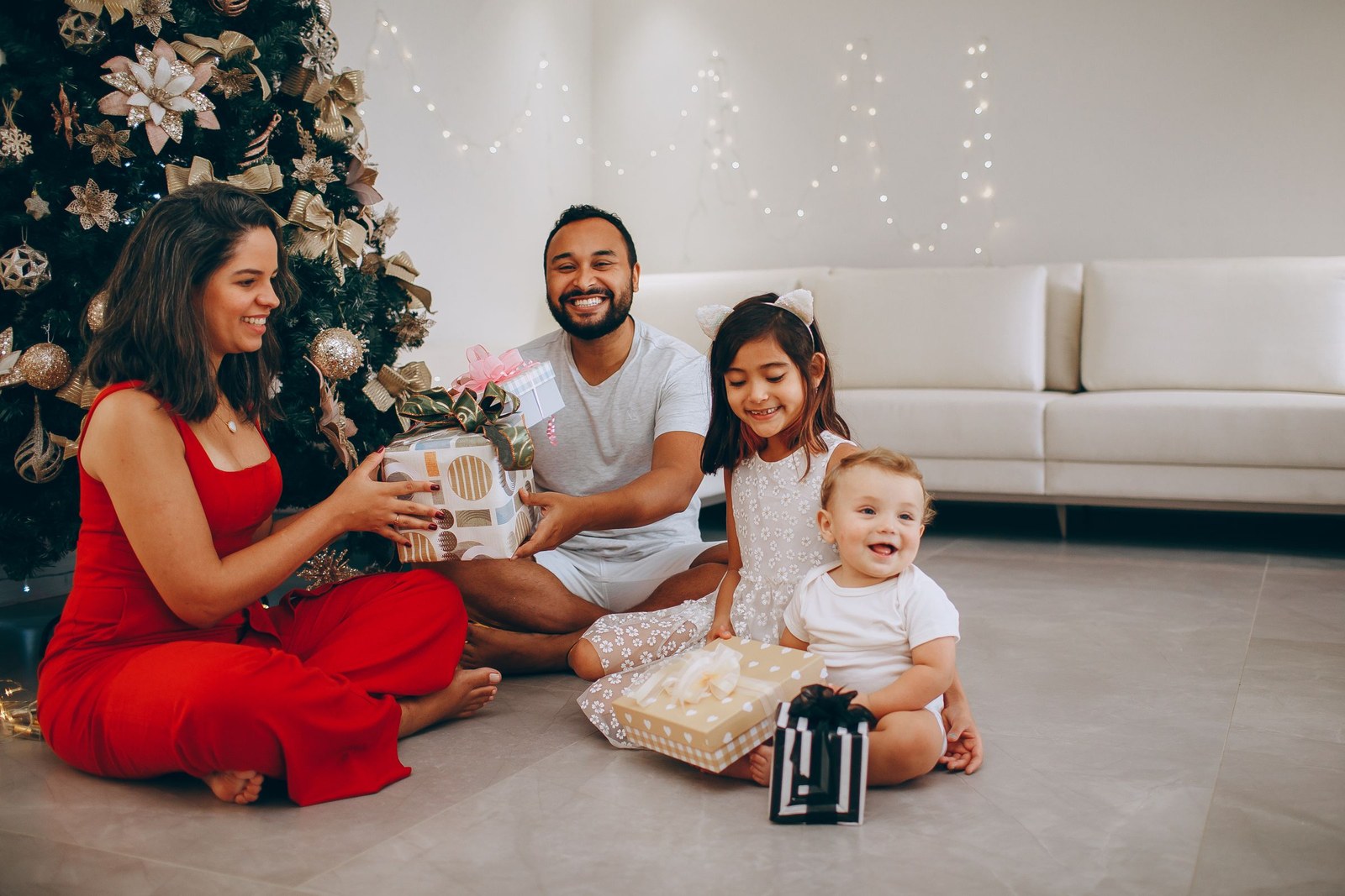 Family smiling warmly while sitting around the Christmas tree with gifts