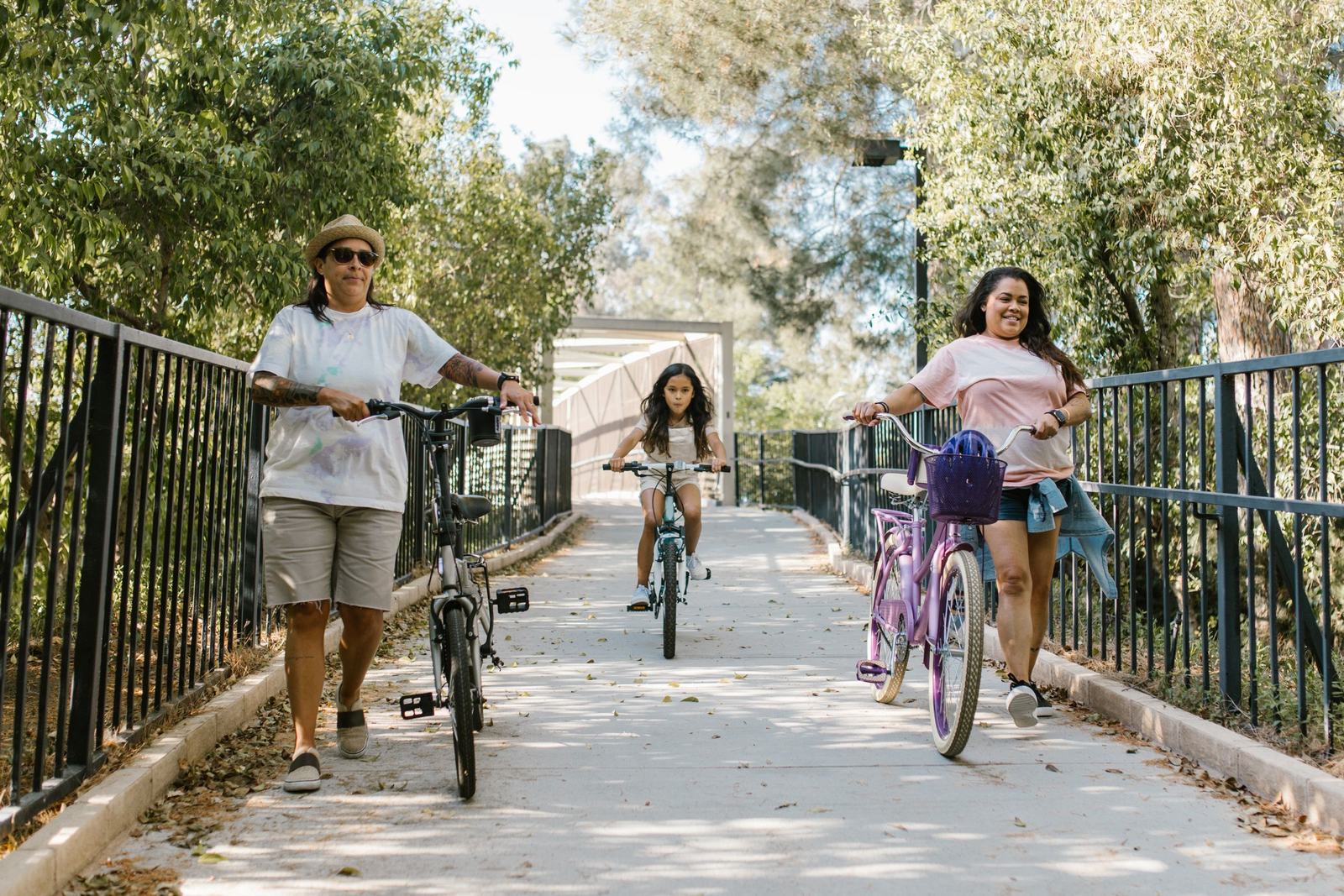 Family walking and riding bicycles together down a sunny park bridge pathway
