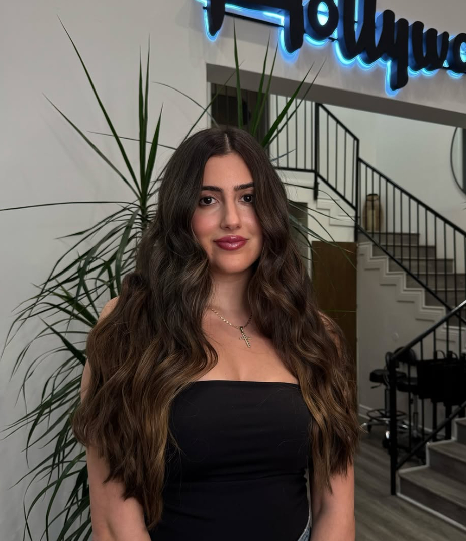 Client with long, full hair extensions under the lit Hollywood neon sign