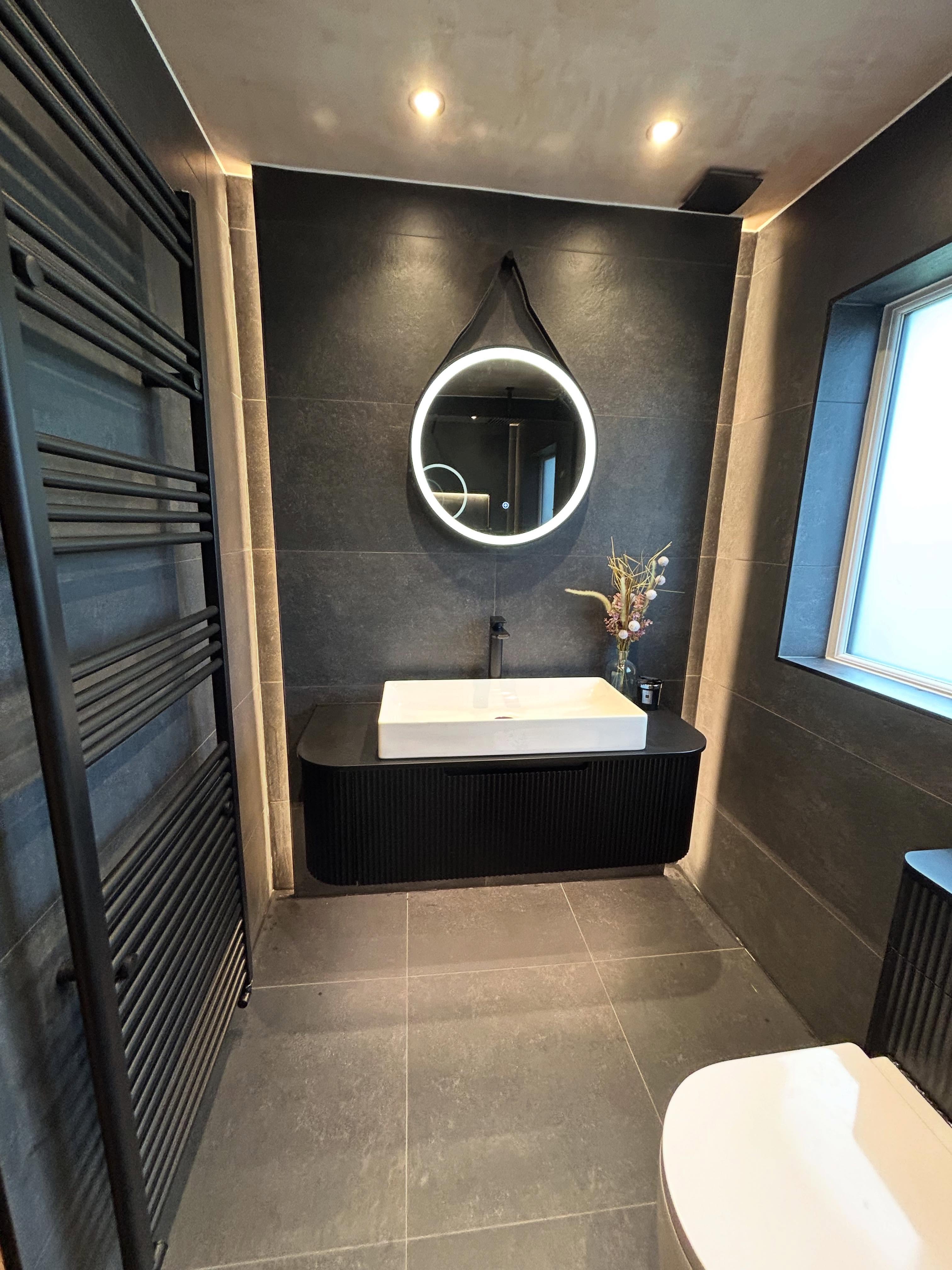 Moody dark charcoal slate bathroom suite with curved fluted black floating vanity, strap-hung halo mirror and matte black fixtures