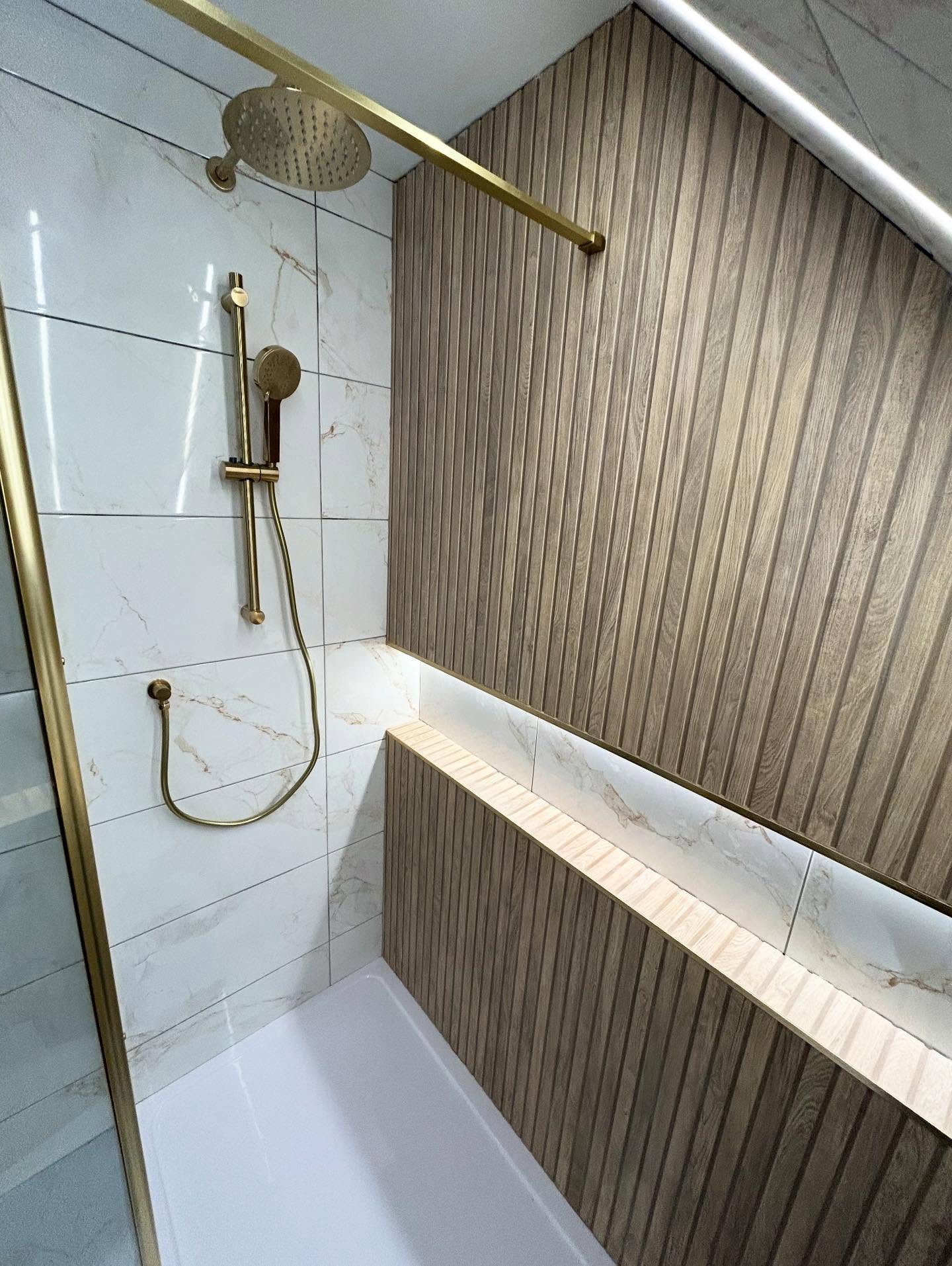 Vaulted eaves loft walk-in shower with vertical wood slat wall, Calacatta gold veined marble tiles, warm illuminated ledge and brushed gold shower hardware