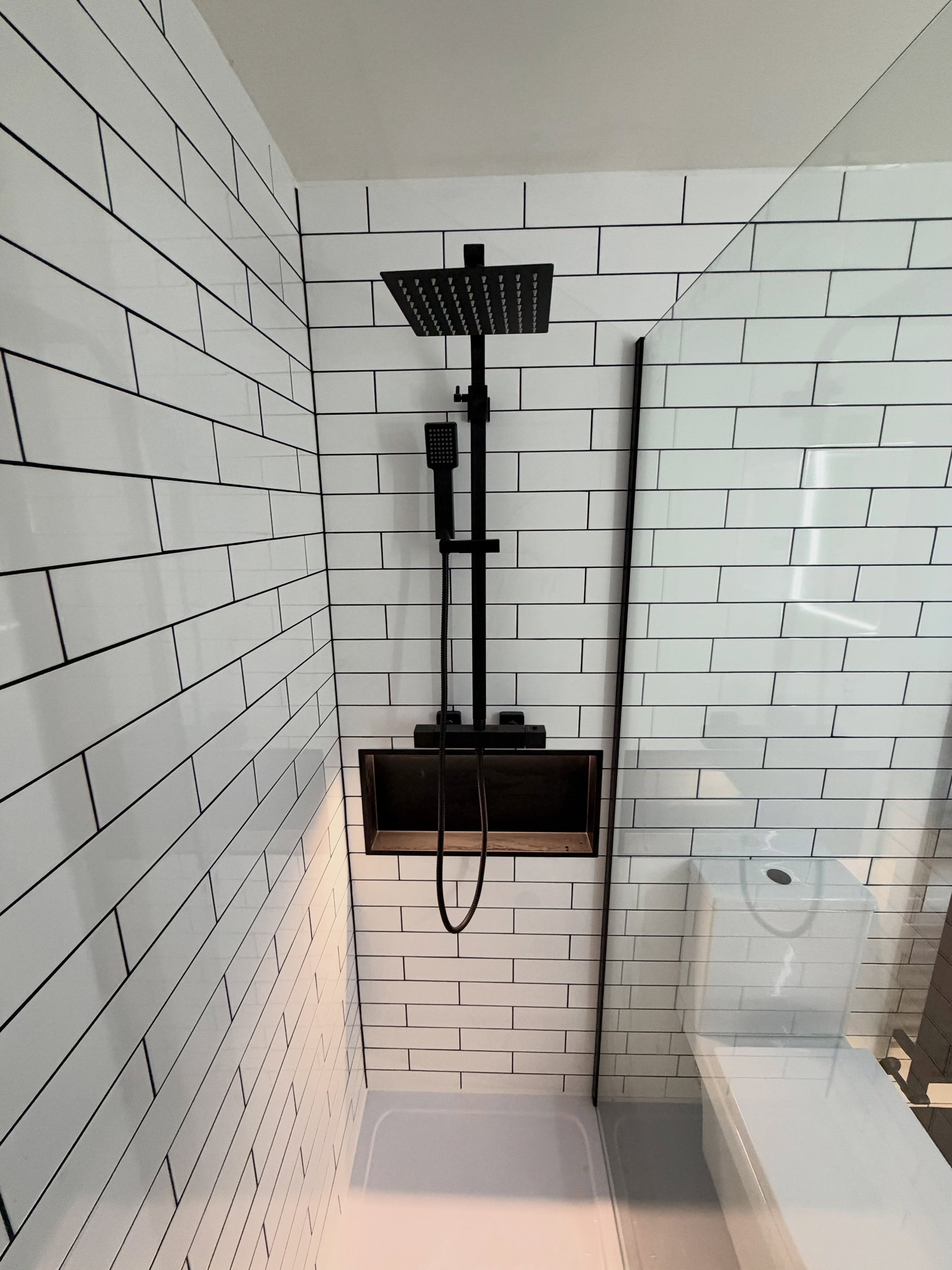 Walk-in shower enclosure with white brick metro tiles, black grout, black thermostatic rainfall shower and illuminated niche