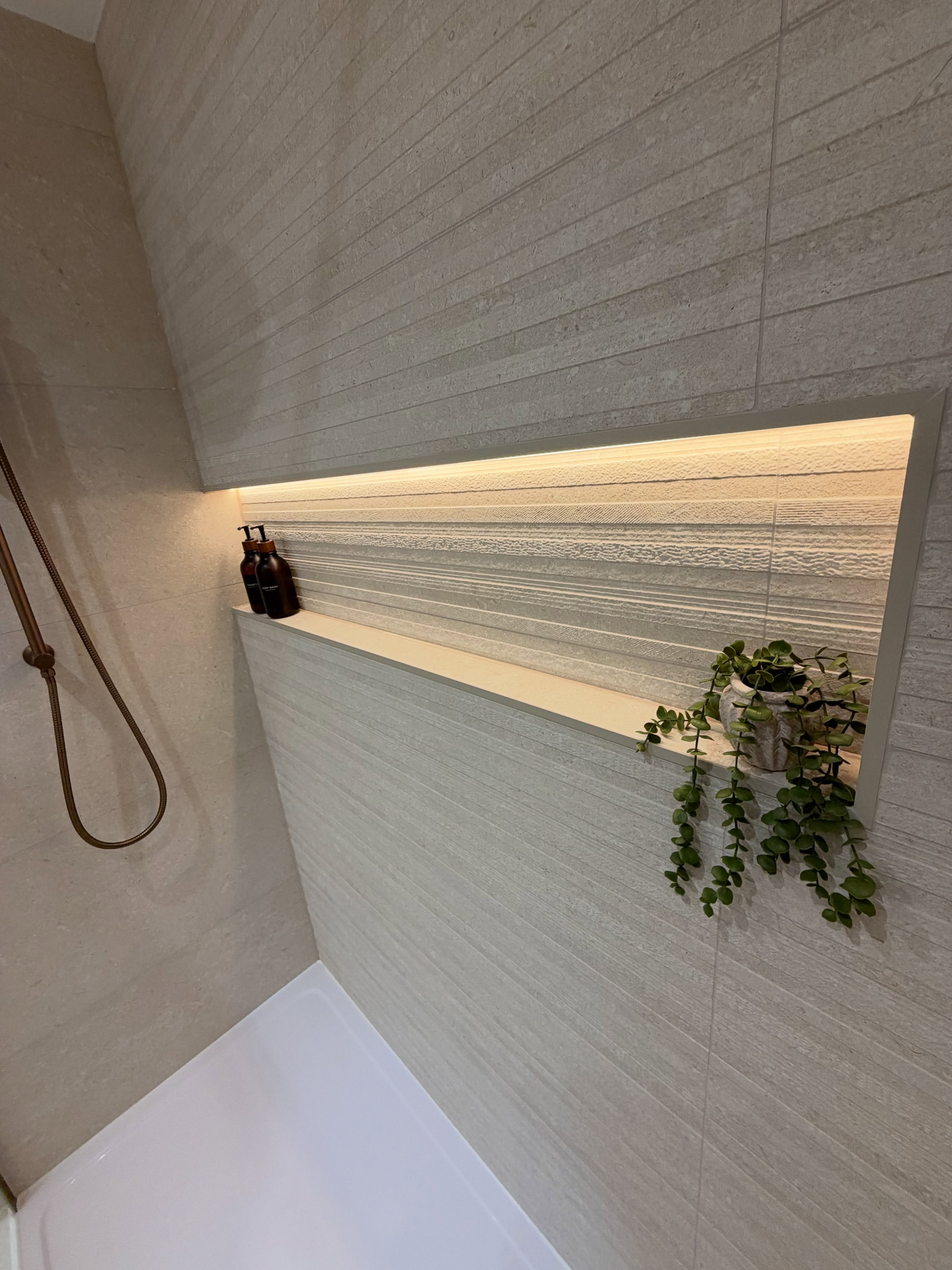 Textured fluted shower wall with illuminated recessed shelf niche and brass shower handset