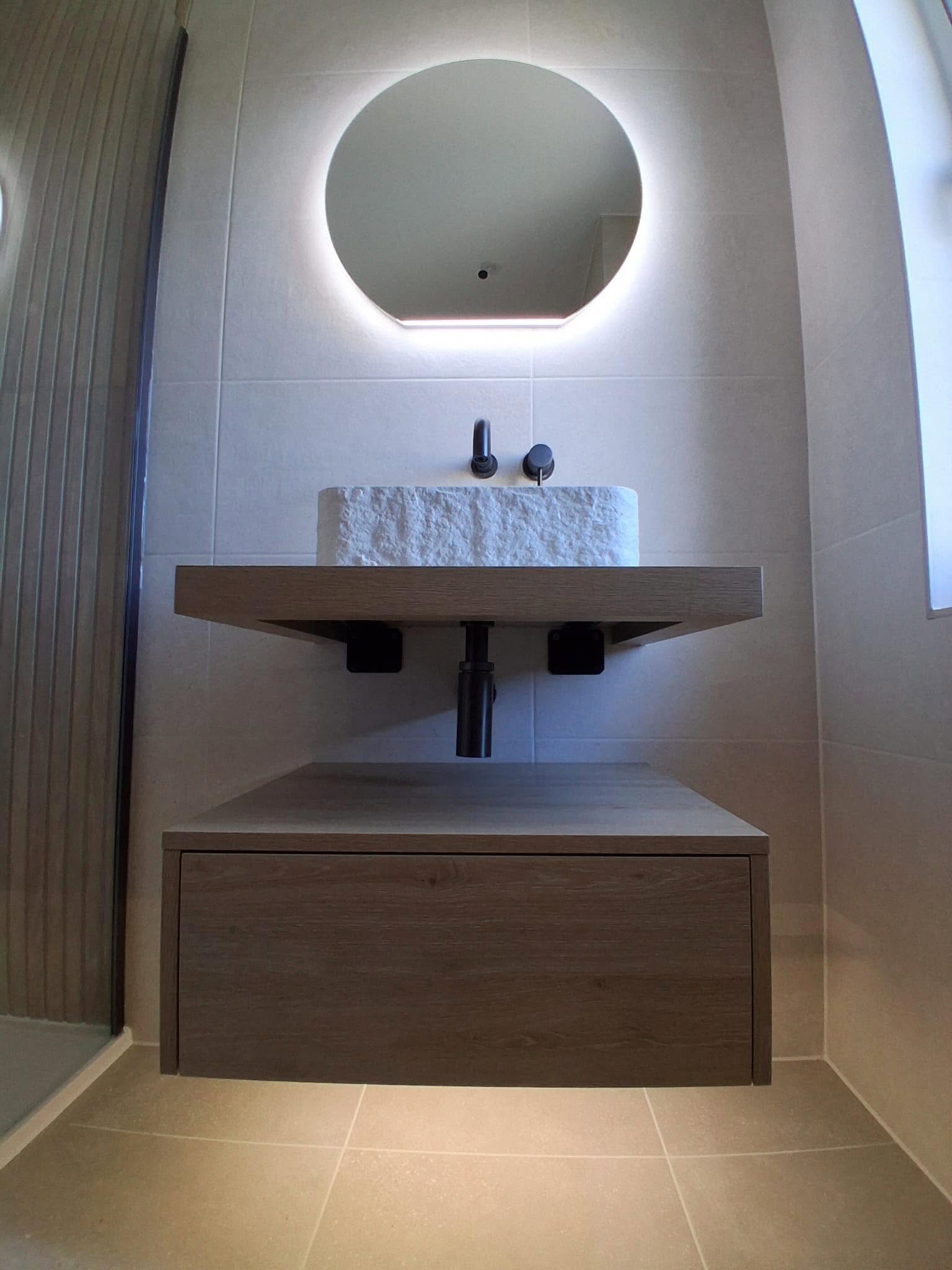 Floating oak two-tier vanity unit with chiseled raw stone vessel basin, matte black wall-mounted tap and illuminated circular halo mirror