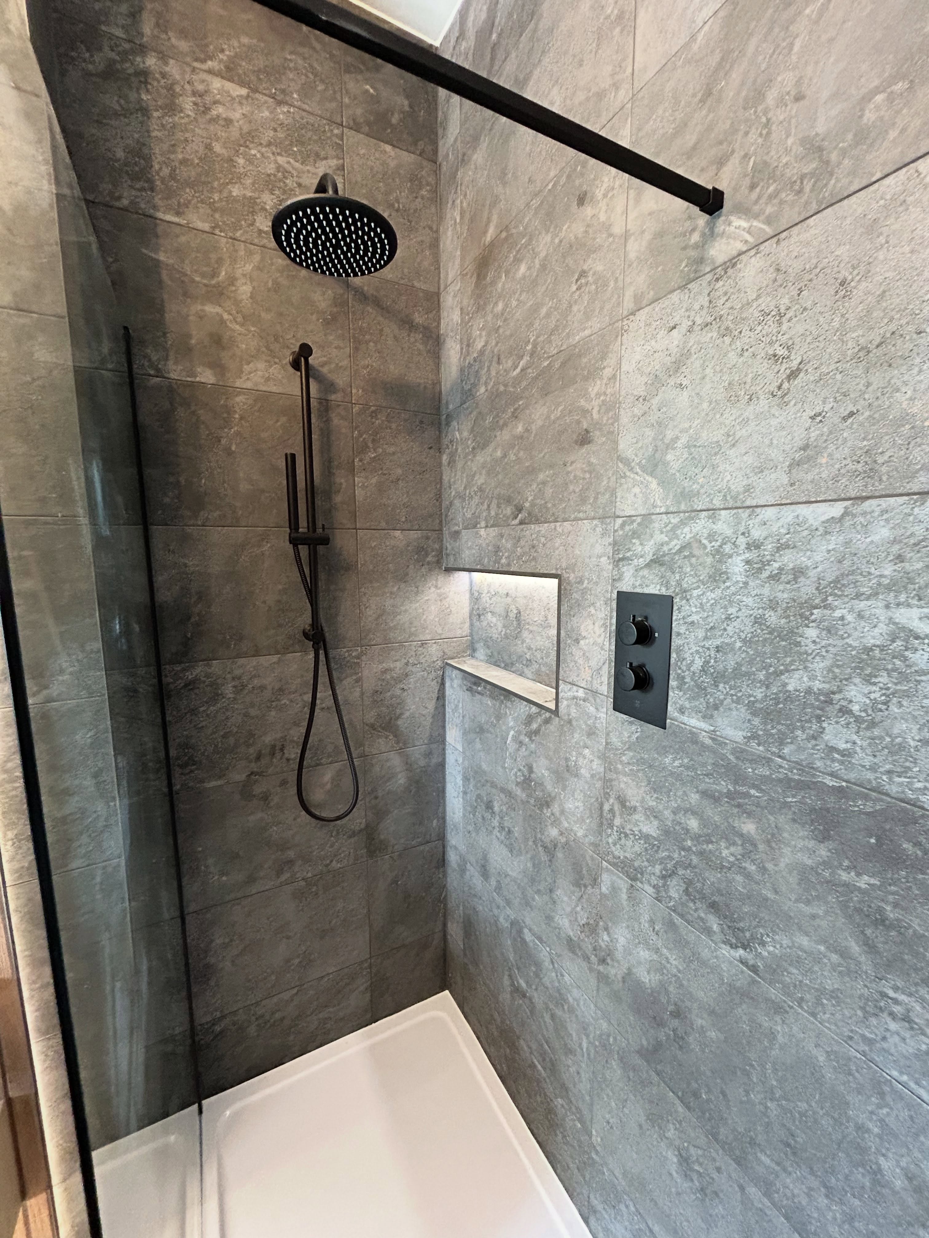 Walk-in shower enclosure with slate grey textured porcelain tiles, illuminated recessed shampoo niche and matte black thermostatic shower system