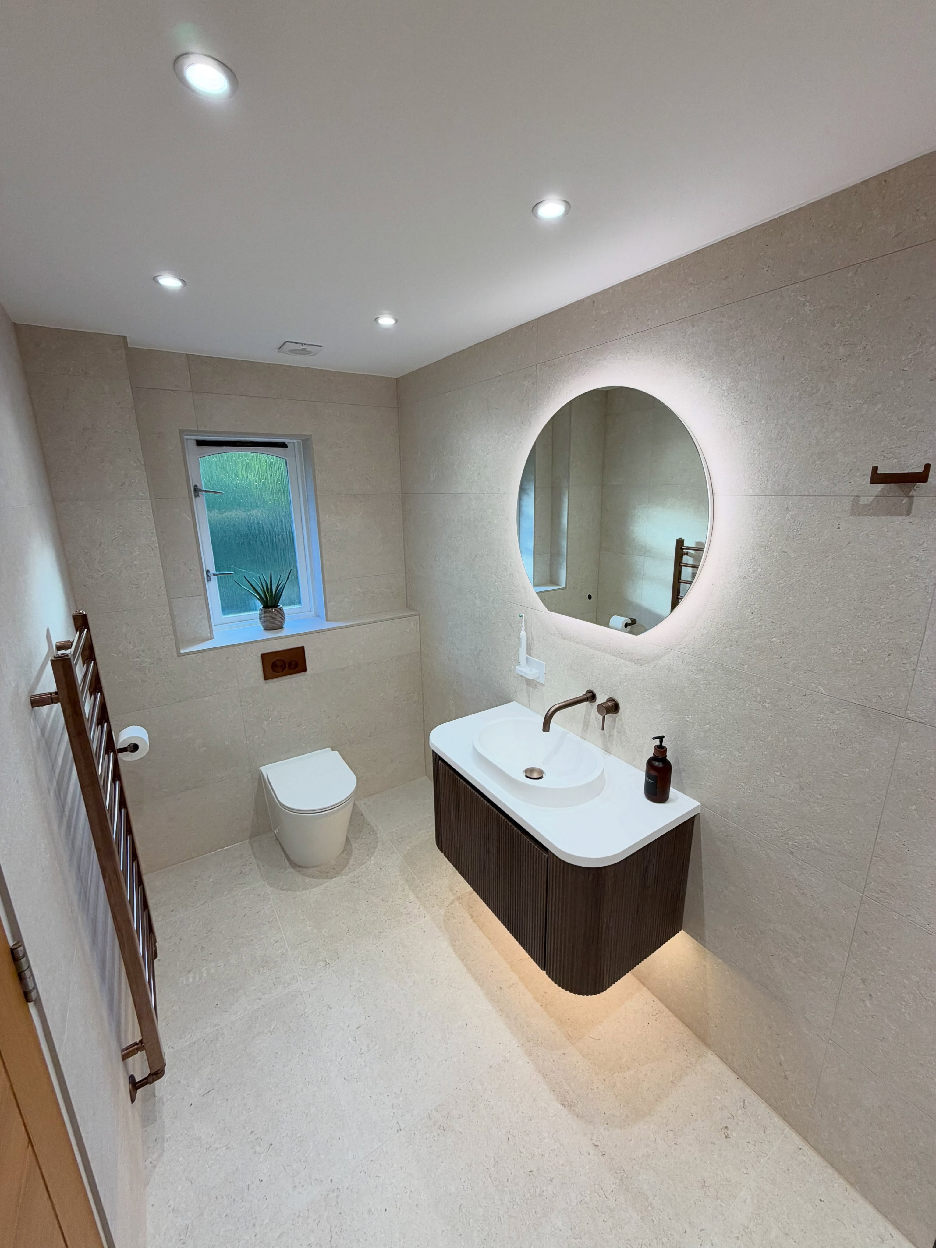 Luxury travertine ensuite with fluted wood vanity and halo mirror in Paisley