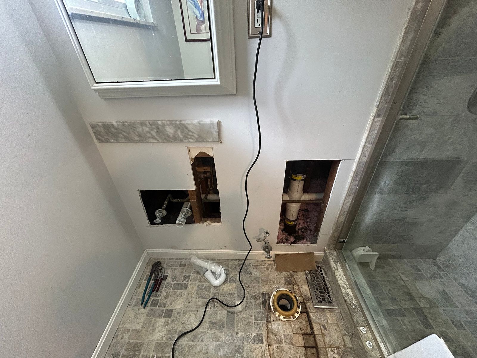 Copper supply lines, shutoff valves and a PVC drain stub exposed behind a bathroom wall