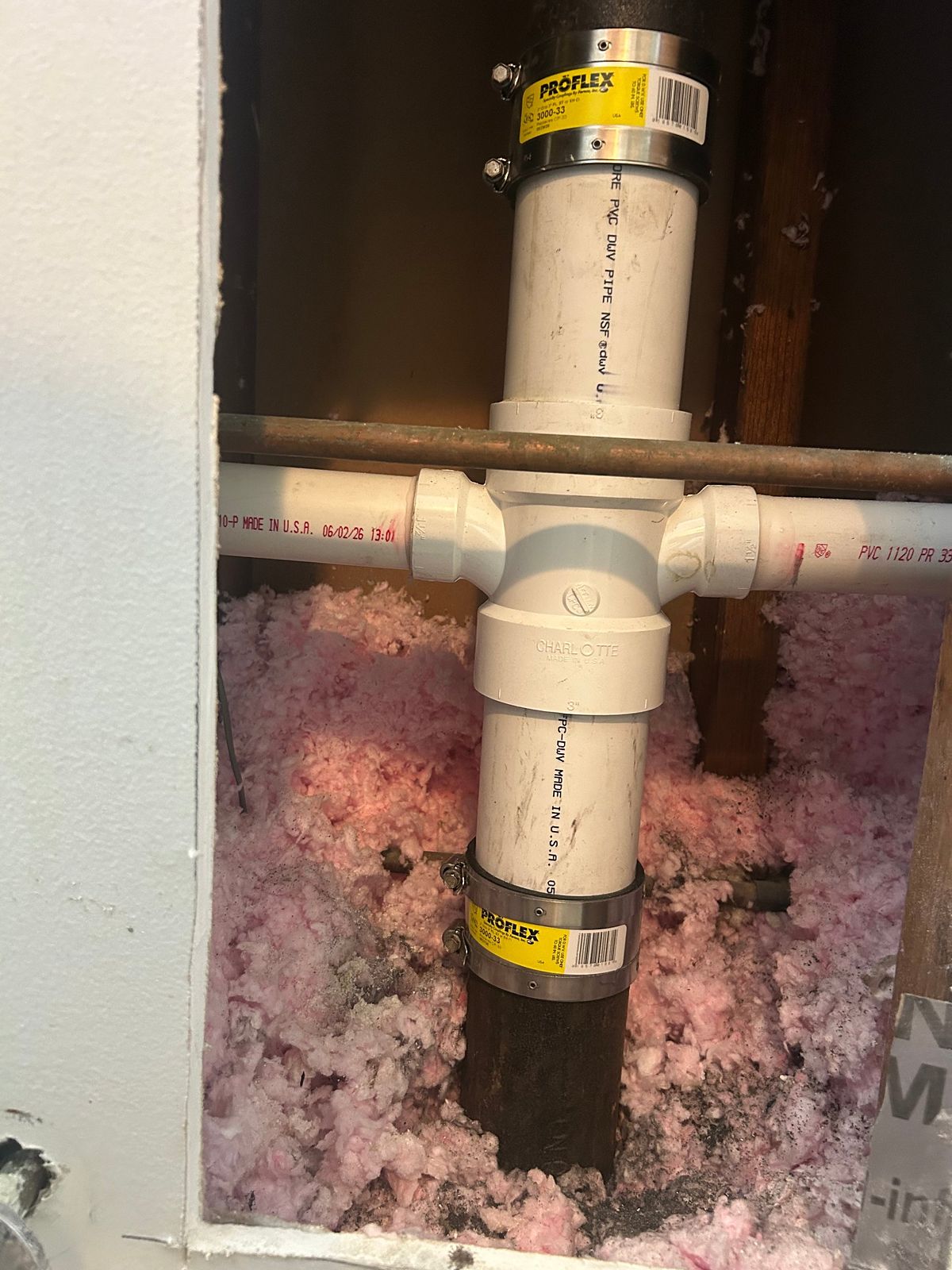 New PVC section joined to an old cast-iron drain stack inside an opened bathroom wall