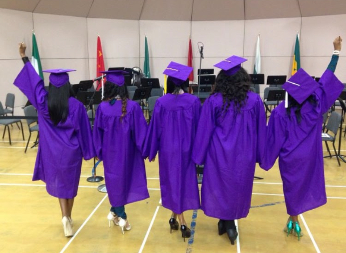Black women college graduates in purple graduation gowns and caps celebrating with hands raised