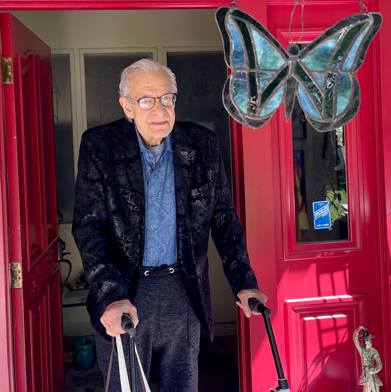 Lanny standing in the doorway with his walker beneath a stained glass butterfly