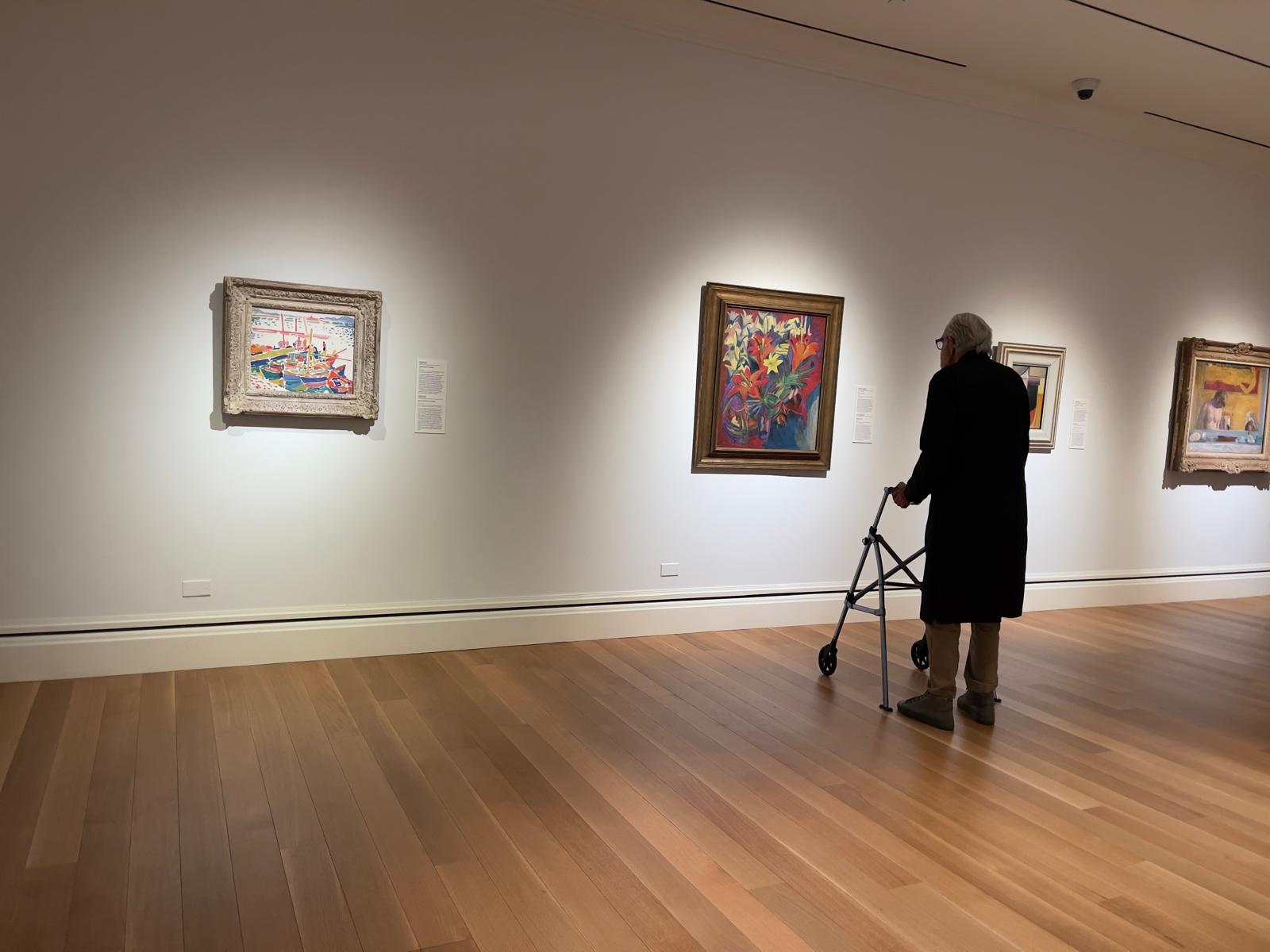 Lanny walking through the sunlit museum gallery among framed masterpieces